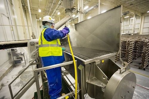 Technician in protective gear cleaning industrial machinery